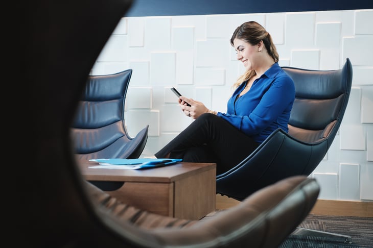 Happy-Business-Woman-With-Smartphone-Sitting-In-Office-Waiting-Room-1132139097_1257x837