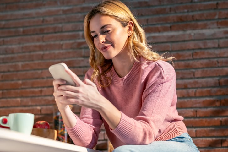 female-european-adult-outdoor-smiling-and-using-her-mobile-phone-in-the-kitchen-web